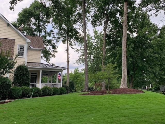 Suburban house with a porch, American flag, and tall trees beside a manicured green lawn