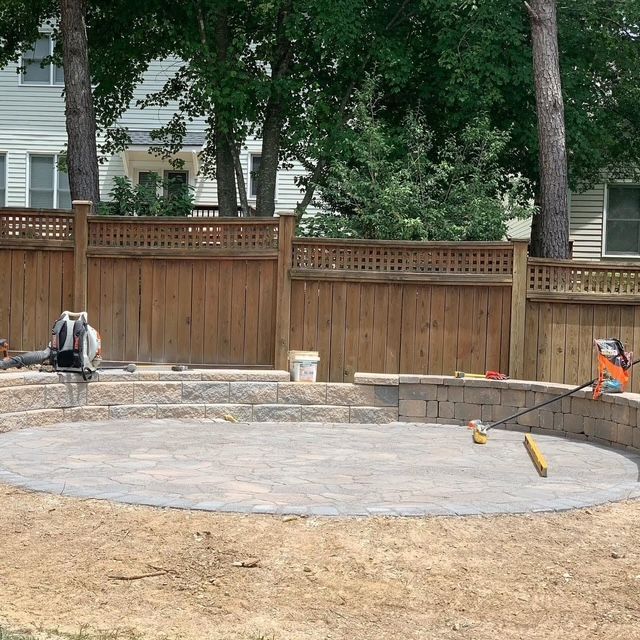 Backyard patio under construction with a curved stone seating wall and tools on the ground