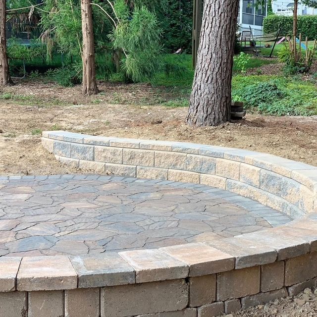 Curved stone retaining wall around a paved patio in a wooded yard