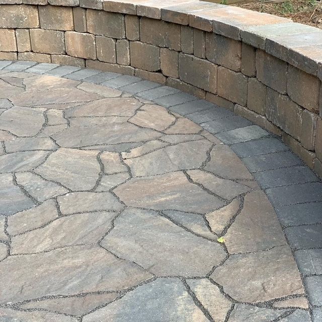 Curved stone patio with irregular flagstones and a low tan brick retaining wall