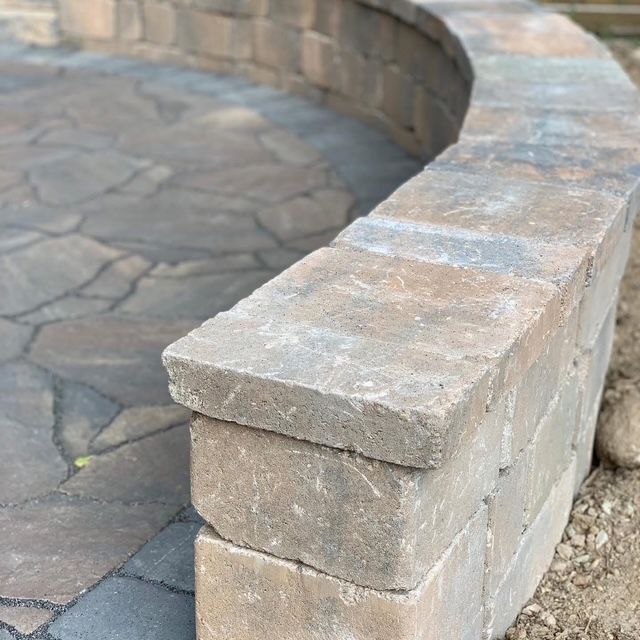 Curved stone retaining wall with beige block cap around a paved patio area