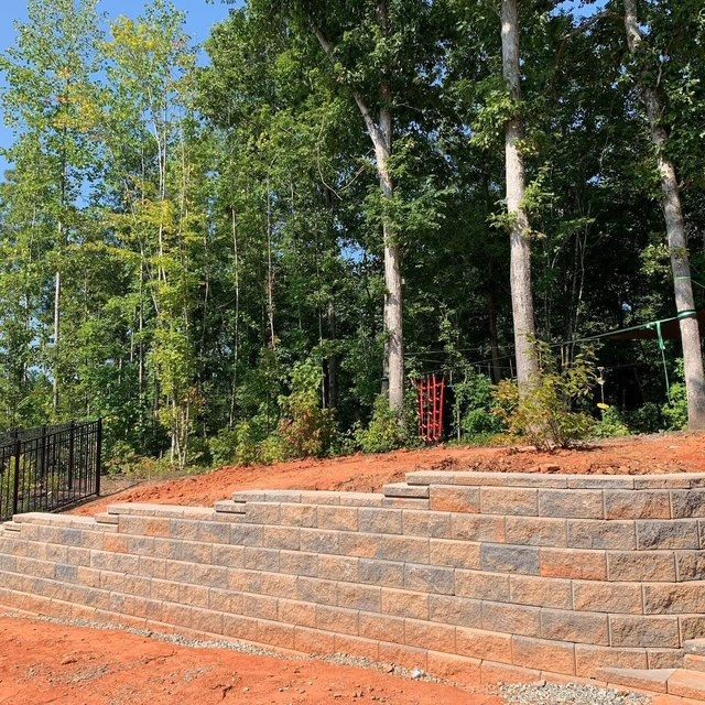 Stone steps beside a wooded yard with tall trees and a black fence under a clear blue sky