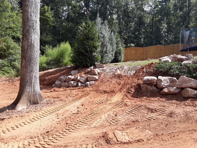 Dirt road cut through a wooded hillside with rock retaining walls and a wooden fence above.