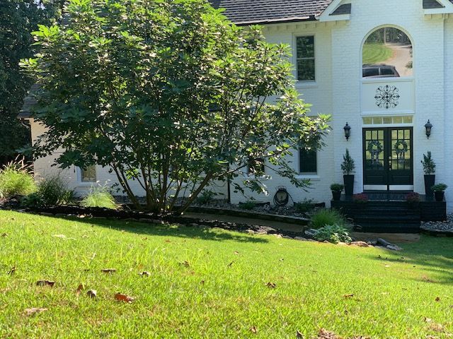 White house with large arched entry, black front door, and green lawn in front.