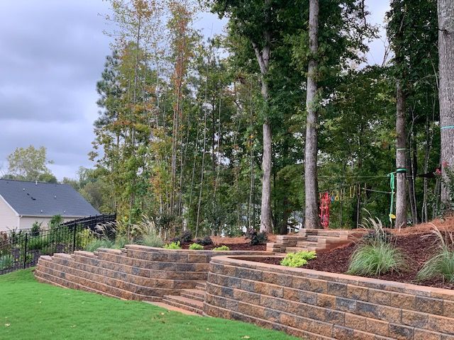 Terraced stone retaining wall with steps and trees in a landscaped backyard