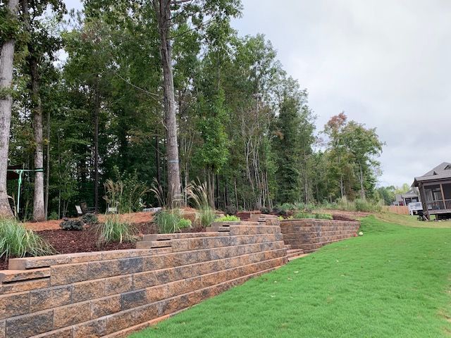 Retaining wall terraced with plants beside a green lawn and trees near a house