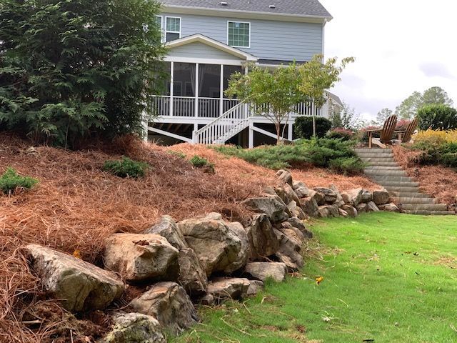 House with front porch, stone retaining wall, and landscaped sloped yard with stairs