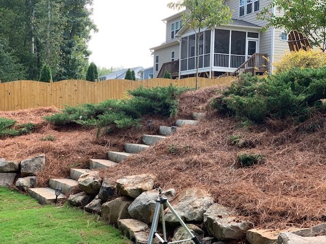 Stone steps climb a landscaped slope beside a house with fresh mulch and shrubs