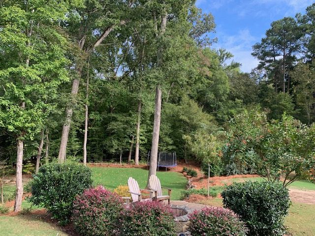 Garden patio with white chairs and a table amid greenery and tall trees