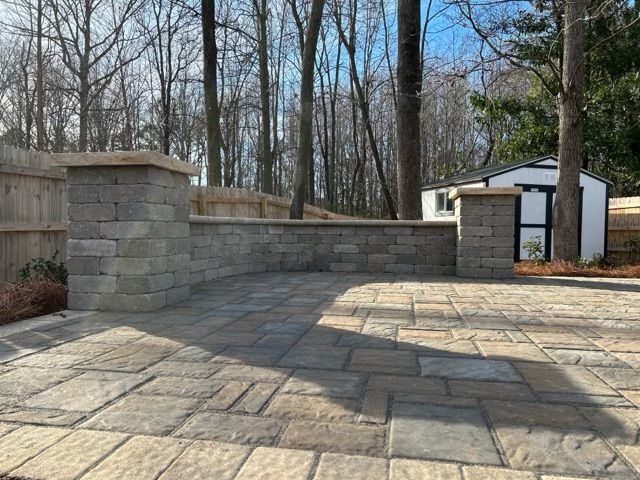 Stone-paved patio with a low retaining wall and trees in the background