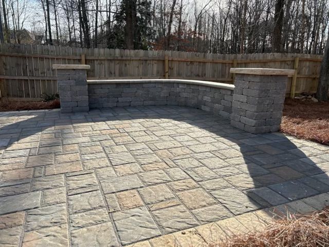 Stone patio with built-in curved bench and brick pillars in a fenced backyard
