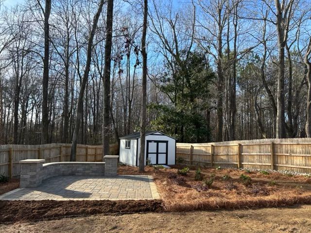 Backyard with stone patio, white shed, and wooden fence under leafless trees