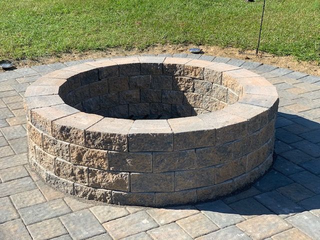 Round stone fire pit in a paved patio beside a grassy lawn