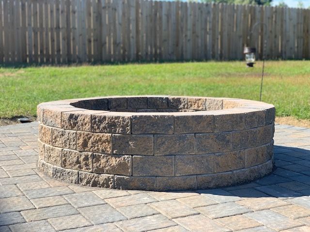 Stone fire pit in a paved backyard with a wooden fence in the background