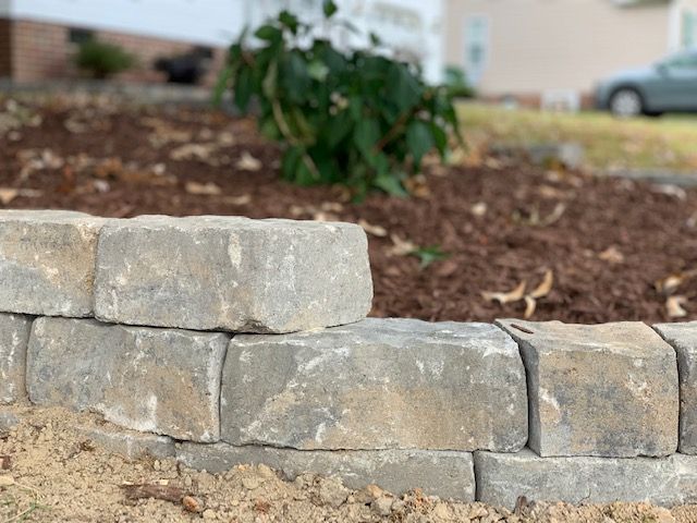 Stone retaining wall blocks in a landscaped yard with mulch and plants