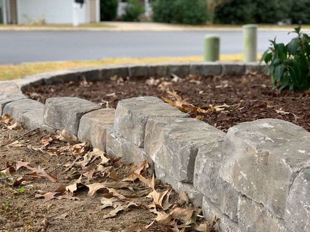 Stone border edging a mulched garden bed beside a road, with fallen leaves in the foreground.