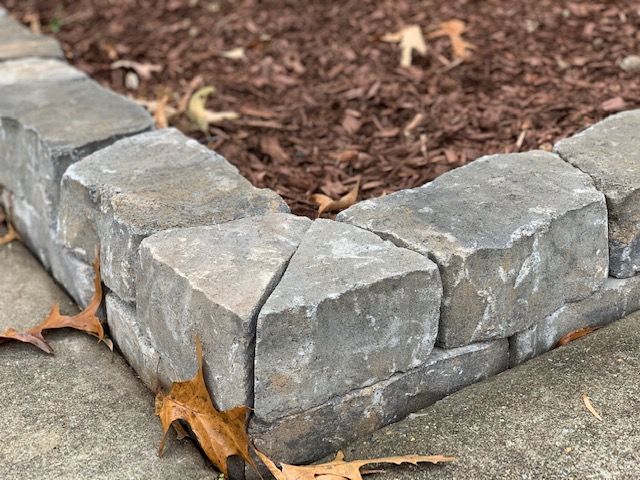Gray stone retaining wall corner edging a landscaped bed with brown mulch and fallen leaves