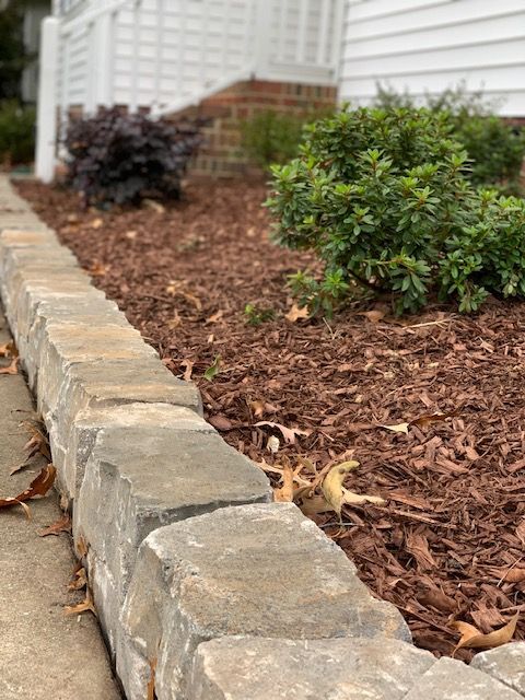 Stone garden border edging a mulched landscape bed with small shrubs.