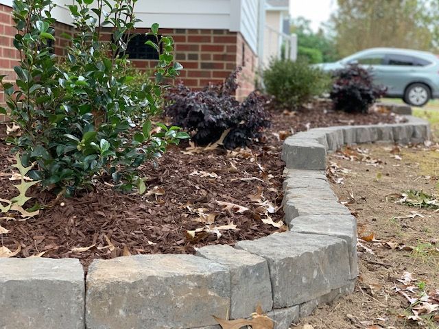 Curved stone garden border with mulch beds and small shrubs beside a house driveway