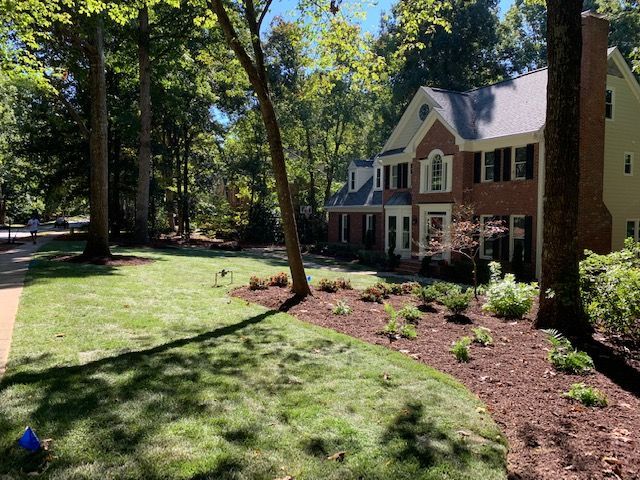 Brick house with white trim and landscaped front yard beside a tree-lined street