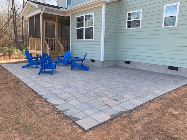 Blue patio chairs on a stone patio beside a light green house with a small porch.