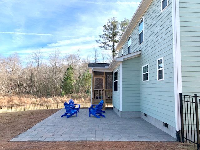 Patio with blue chairs beside a light blue house and screened porch on a paved backyard terrace
