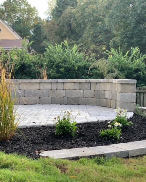 Backyard patio with a curved stone retaining wall, paver floor, and small flower beds