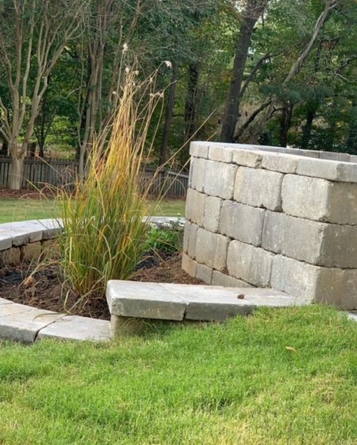 Stone garden seating beside a small planter with tall grasses in a grassy backyard