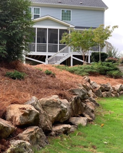 House with screened porch and white stairs above a rocky landscaped slope and green lawn
