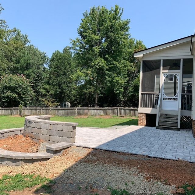 Backyard patio with paver walkway, circular stone fire pit, and screened porch beside a fenced lawn