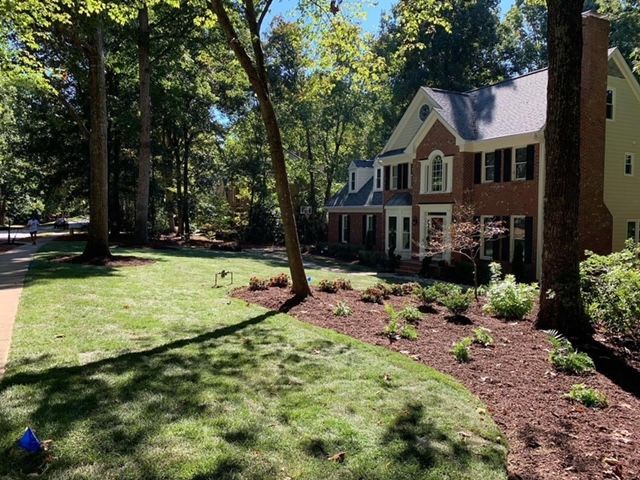 Suburban house with brick and siding, front lawn, trees, and landscaped mulch beds in daylight