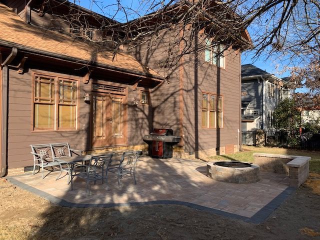 Wooden house exterior with patio chairs, a small grill, and leafless trees in a sunny yard