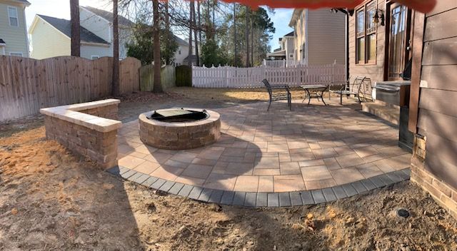 Backyard patio with stone fire pit, brick pavers, bench, and wooden fence beside a house