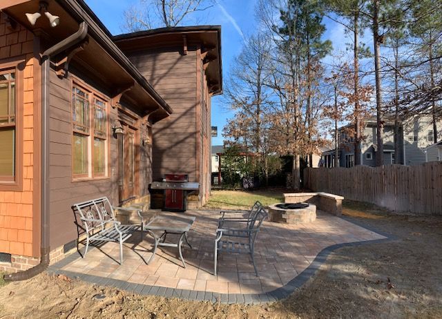 Wooden cabin patio with metal chairs, stone fire pit, and a fenced yard on a sunny day