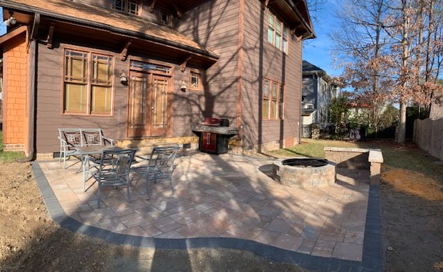 Wooden house patio with outdoor chairs, benches, and a red grill in a sunny yard