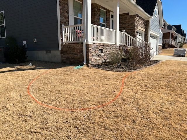 Suburban house front porch with a stone foundation and a marked patch of dry grass in the yard