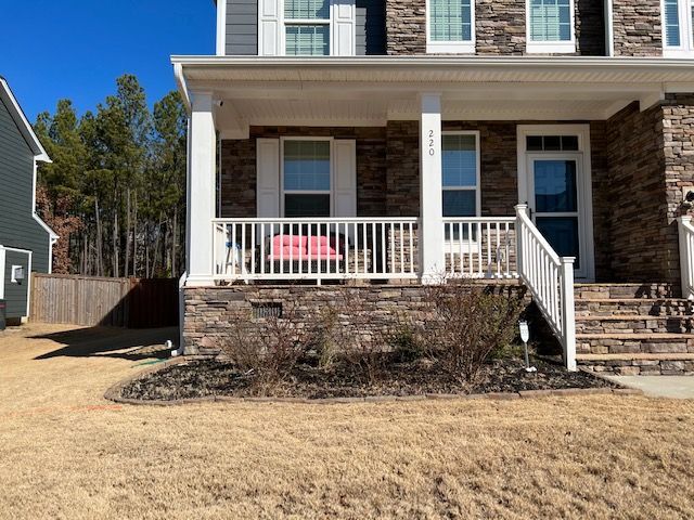 Front porch of a brick house with white railings, steps, and a pink chair on the porch.