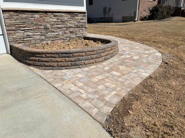 Curved stone paver walkway beside a brick house and raised stone planter