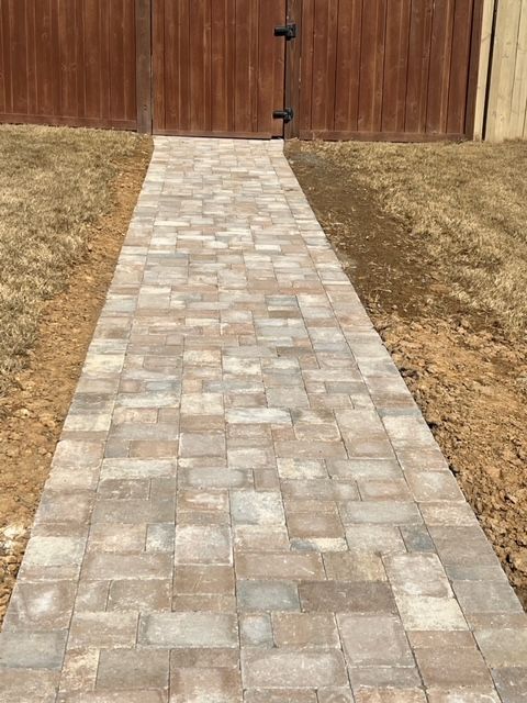 Brick walkway leading to a wooden gate, bordered by dry grass.