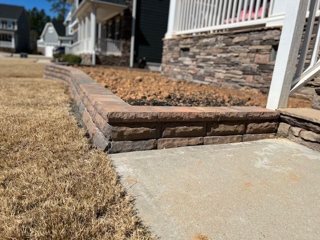 Stone steps beside a brick house, leading from a concrete sidewalk to a dry, brown lawn.