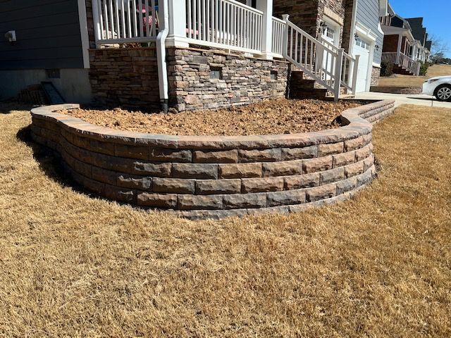 Curved stone retaining wall with mulch beside a house porch and dry grass lawn