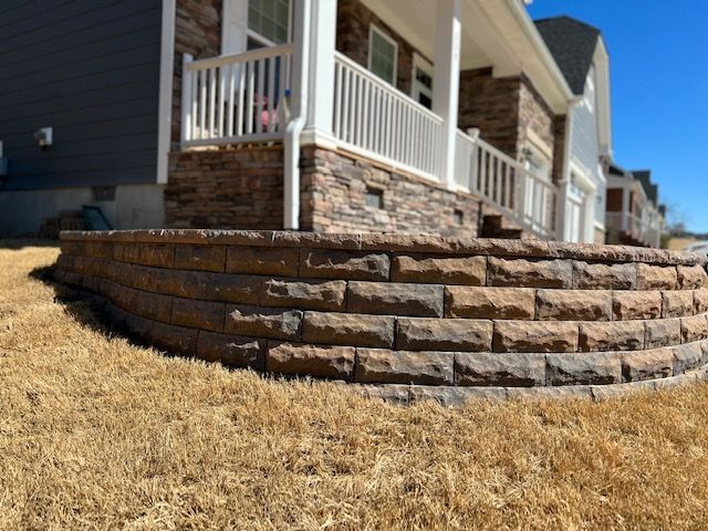 Stone retaining wall supporting a white porch beside a dry, grassy yard