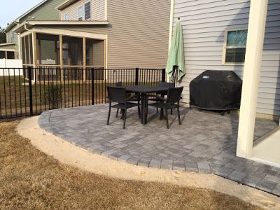 Backyard patio with black table and chairs, grill, umbrella, and fenced lawn beside a house