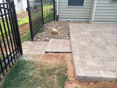 Backyard patio with stone pavers, a fenced walkway, and patchy grass near a house.