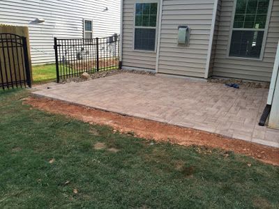 Brick patio beside a house with a black metal fence and a small lawn in the foreground