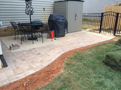 Patio with outdoor table, covered grill, storage shed, and paver walkway beside a grassy yard