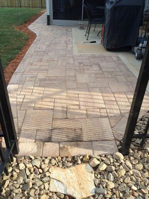 Paver patio leading to a covered outdoor area, bordered by rocks and grass.