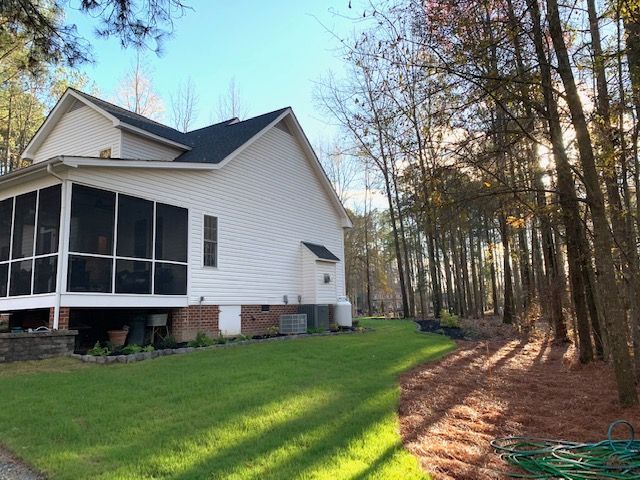 White house with screened porch beside a wooded yard in late-afternoon light