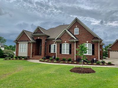 Brick suburban house with manicured lawn and cloudy sky