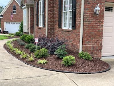 Brick house front walkway with curved mulched flower bed and small shrubs along the foundation